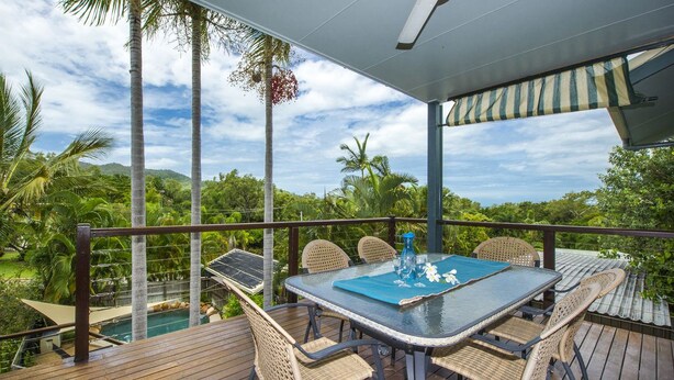 A wooden deck with a glass table and wicker chairs, overlooking a pool and lush greenery. - Manyana (Nelly Bay)