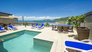 A rooftop pool area with blue lounge chairs, a small pool, and a view of the sea. - 1 Bright Point Apartment 1503 (Nelly Bay)