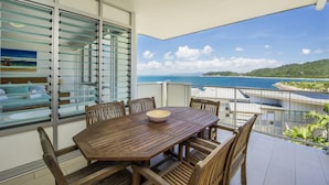 A dining area with a wooden table and chairs, a glass partition, and a view of the sea. - 1 Bright Point Apartment 1503 (Nelly Bay)