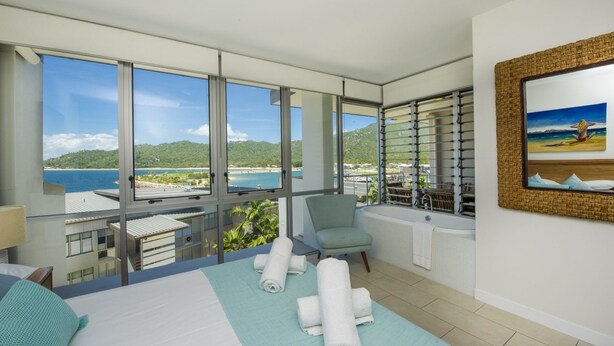 A hotel room with a large balcony, a bed with towels, a chair, and a painting on the wall. - 1 Bright Point Apartment 1503 (Nelly Bay)