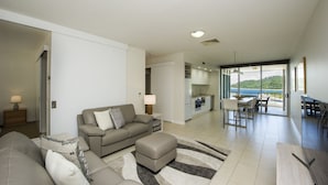 A modern living room with a sofa, ottoman, and a dining area with a view of the sea. - 1 Bright Point Apartment 1503 (Nelly Bay)