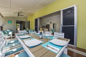 A dining area with a long table set for a meal, a sofa, and a view of the kitchen and outdoor area. - Azur Villa (Horseshoe Bay)