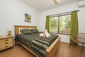A bedroom with a bed, a nightstand, a chair, a window with curtains, and a painting on the wall.