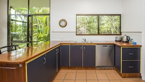 Une cuisine dotée d’un plan de travail en bois, de meubles de rangement sombres, d’un lave-vaisselle et d’une fenêtre donnant sur un paysage verdoyant.