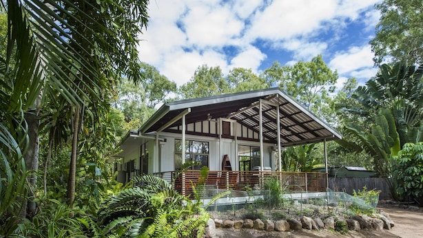 Une maison dotée d’un porche abrité, entourée d’une végétation luxuriante et d’arbres.