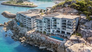 Un hotel frente al mar con varios pisos, una piscina y un litoral rocoso.