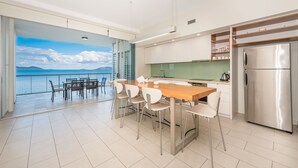 Una cocina moderna con una isla grande, electrodomésticos de acero inoxidable y vista al mar a través de un ventanal.