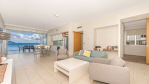 Amplia sala de estar con un gran ventanal que ofrece vista al mar, un comedor y una cocina.