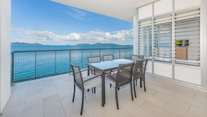 Un balcón con vistas al mar, una mesa con sillas y un televisor a la derecha.
