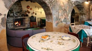 A rustic interior with a stone fireplace, a round dining table with a floral tablecloth, and a sofa. - Villa Nicetta (San Fratello)