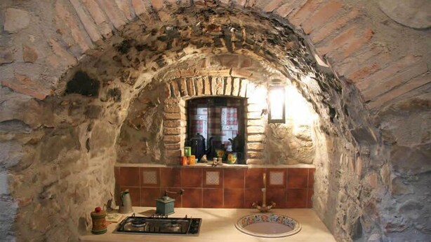 A stone-walled kitchen with a built-in oven, a tiled backsplash, and a window above the counter. - Villa Nicetta (San Fratello)