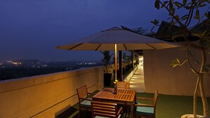 A balcony with a table and chairs, an umbrella, and a view of the cityscape at dusk. - Lemon Tree Hotel, Sector 68, Sohna Road, Gurugram (Gurugram)