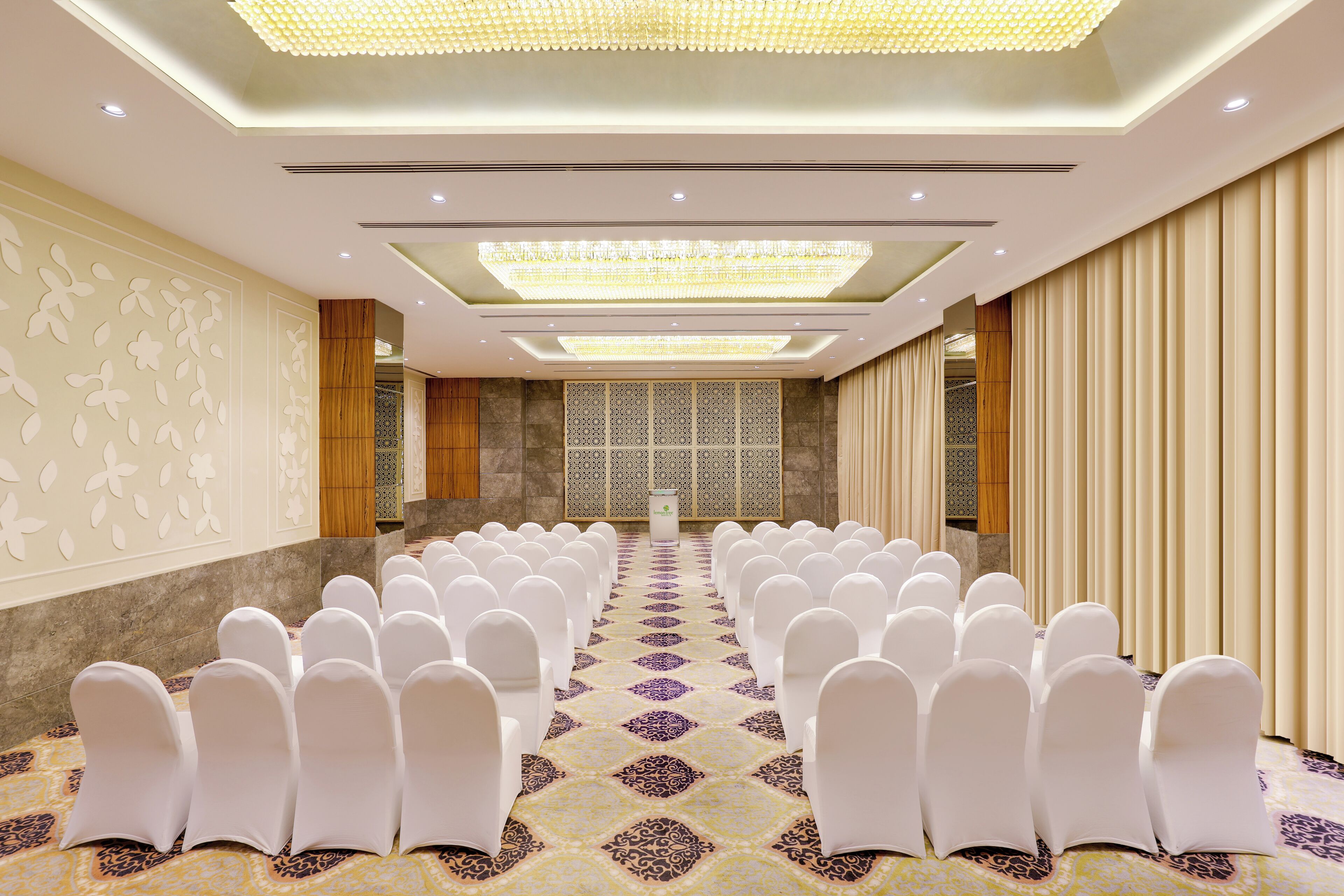 A conference room with rows of white chairs, a patterned carpet, and a large chandelier.