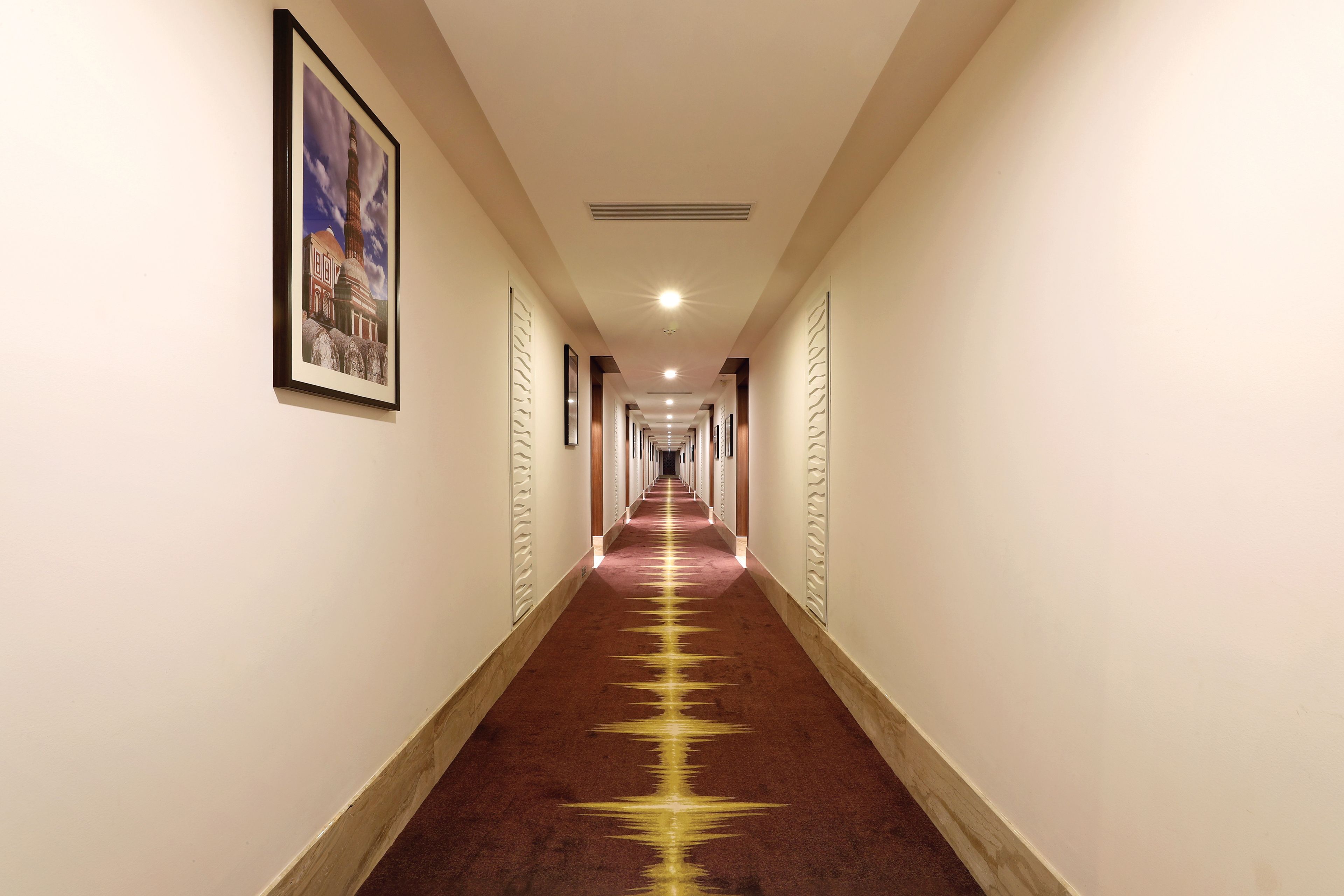 A long, narrow hallway with a red carpet and a framed picture on the left wall.