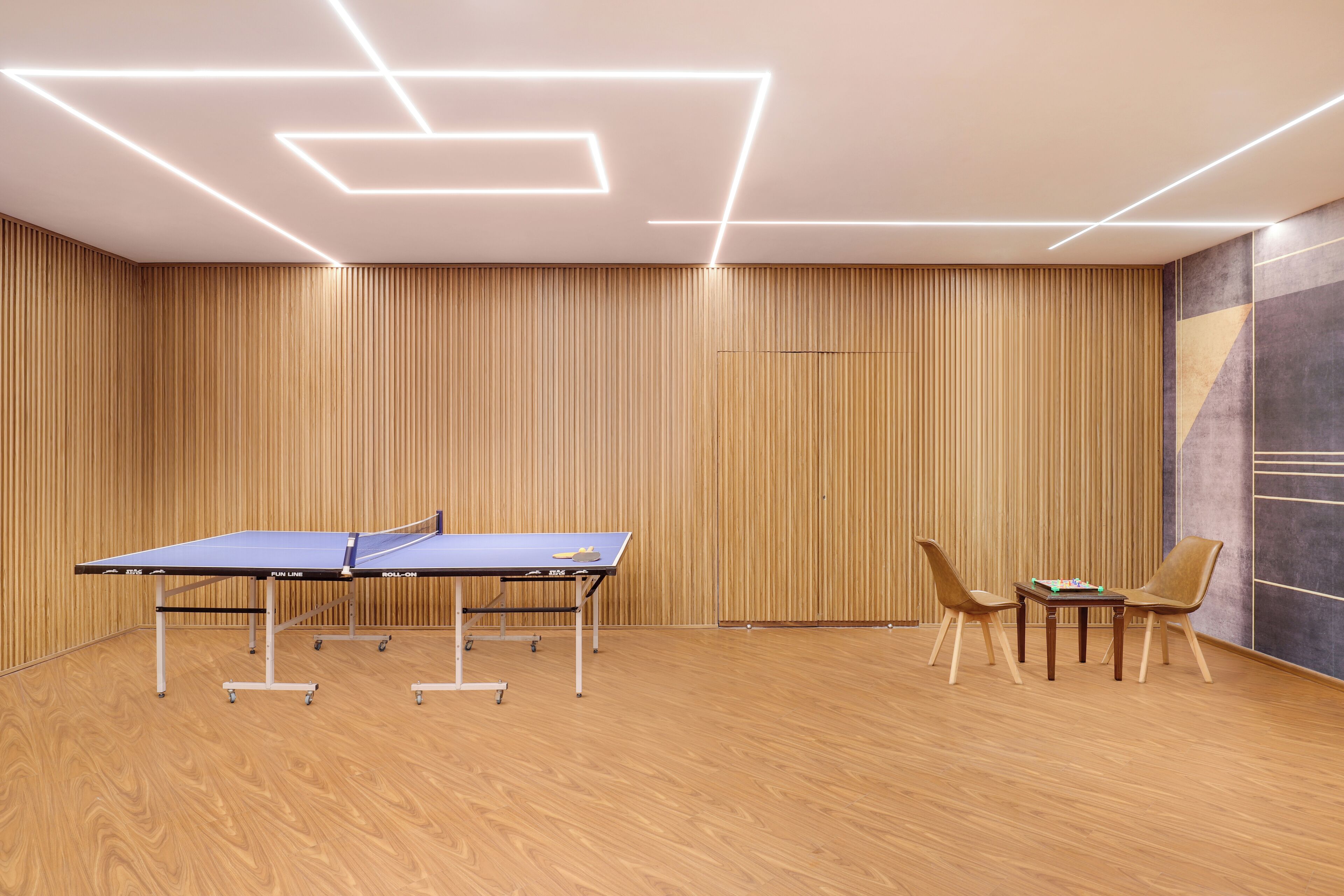 A ping pong table with two chairs, a small table, and a wall with vertical wooden slats.
