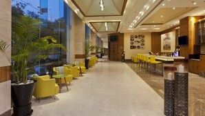A modern hotel lobby with yellow chairs, a reception desk, and a large potted plant. - Lemon Tree Hotel, Sector 68, Sohna Road, Gurugram (Gurugram)