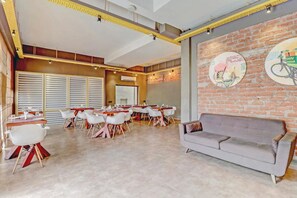 A modern dining area with a brick wall, round tables, and white chairs. - Hotel Beebiz Guindy (Chennai)