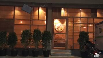 A building with a wooden facade, large windows, and a door with a circular decorative element. There are potted plants in front and a motorcycle parked to the side.