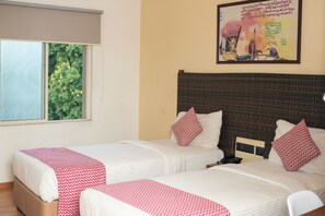 A hotel room with two beds, a window with a view of greenery, and a wall with a framed picture. - Hotel Beebiz Guindy (Chennai)