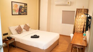 A hotel room with a bed, a desk, a chair, a lamp, a water bottle, and a painting on the wall.