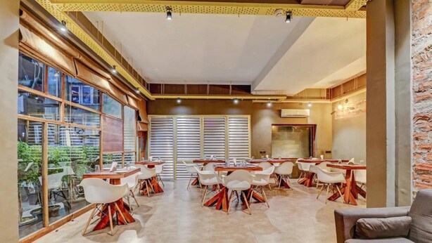 A spacious dining area with multiple tables and chairs, large windows, and a brick wall.