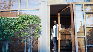 A person standing at the entrance of a building with a wooden door and a window.