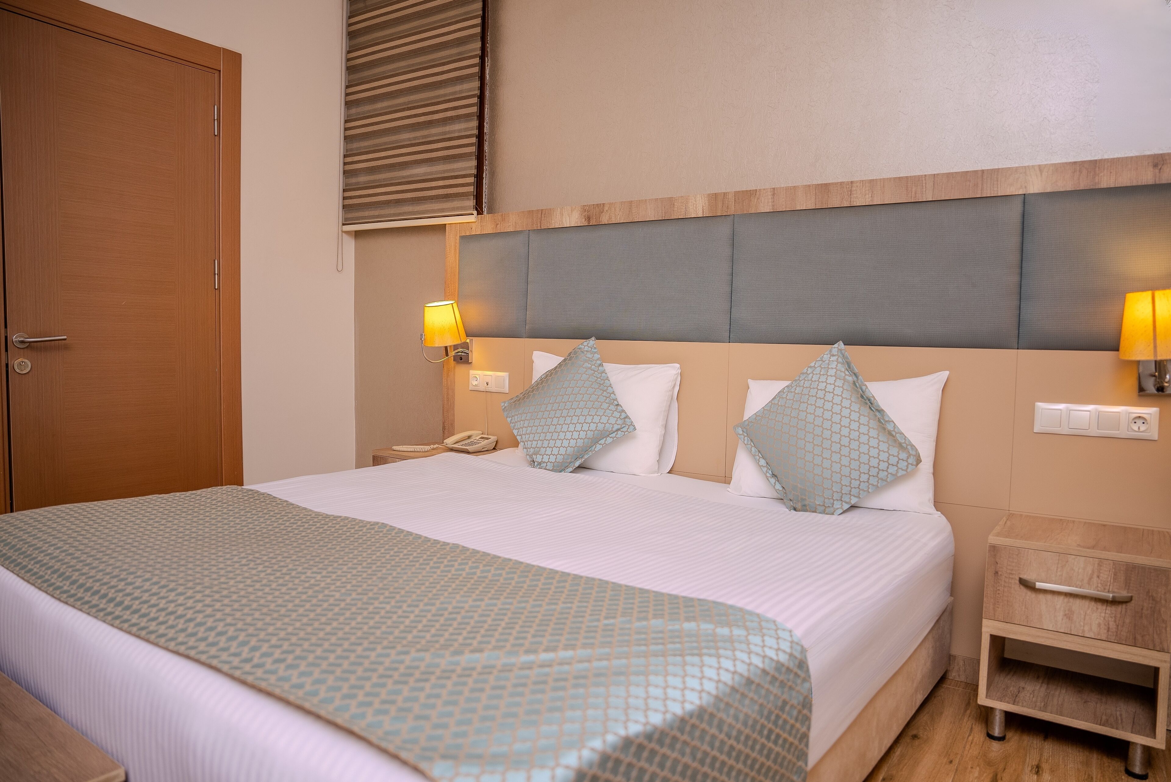 A hotel room with a large bed, bedside lamps, a wooden nightstand, and a door.