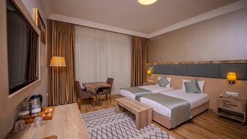 Habitación de hotel con dos camas, un escritorio con una silla, una mesita, una lámpara y una mesita de noche con un teléfono.