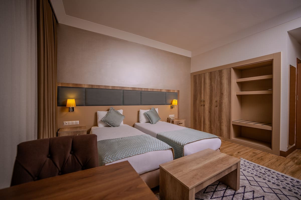 A hotel room with two beds, a wooden wardrobe, a desk, and a chair.