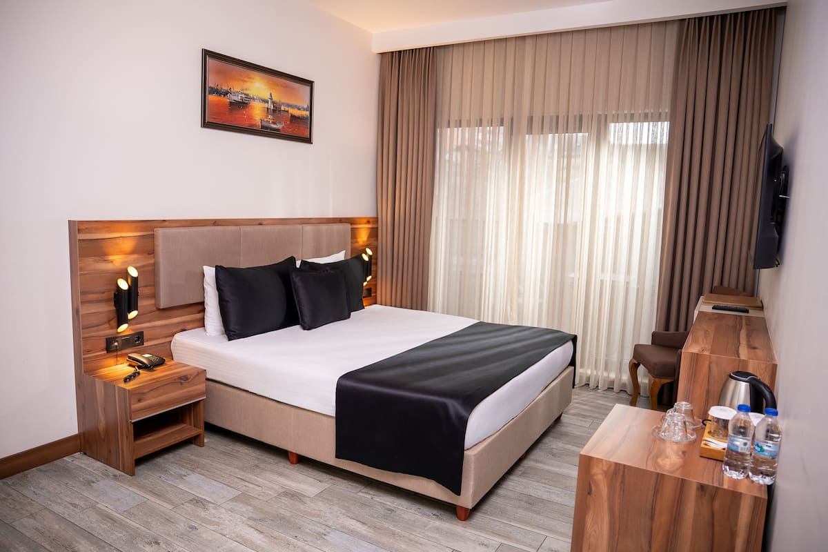 A hotel room with a bed, bedside tables, a desk, a television, and a painting on the wall.