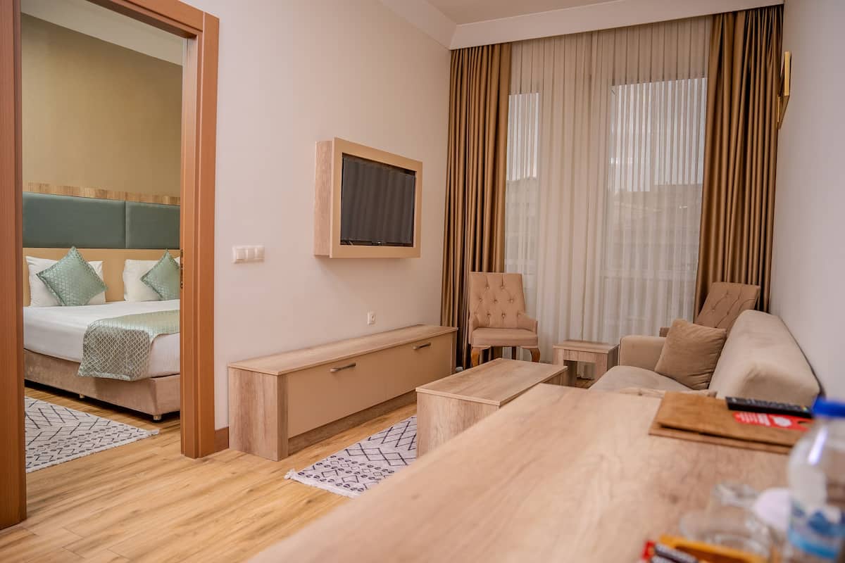 A modern hotel room with a bed, a TV mounted on the wall, a sofa, a coffee table, and a small wooden cabinet.
