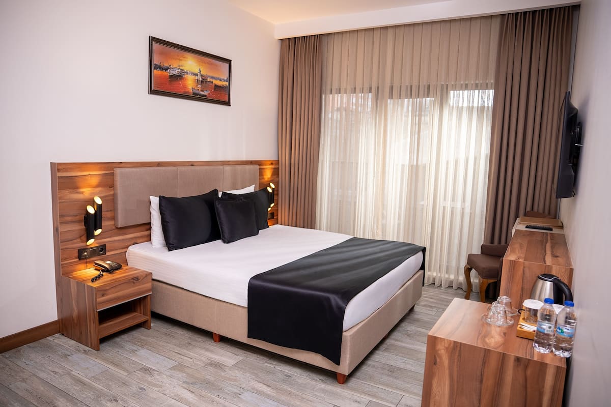 A hotel room with a bed, bedside tables, a desk, a television, and a painting on the wall.