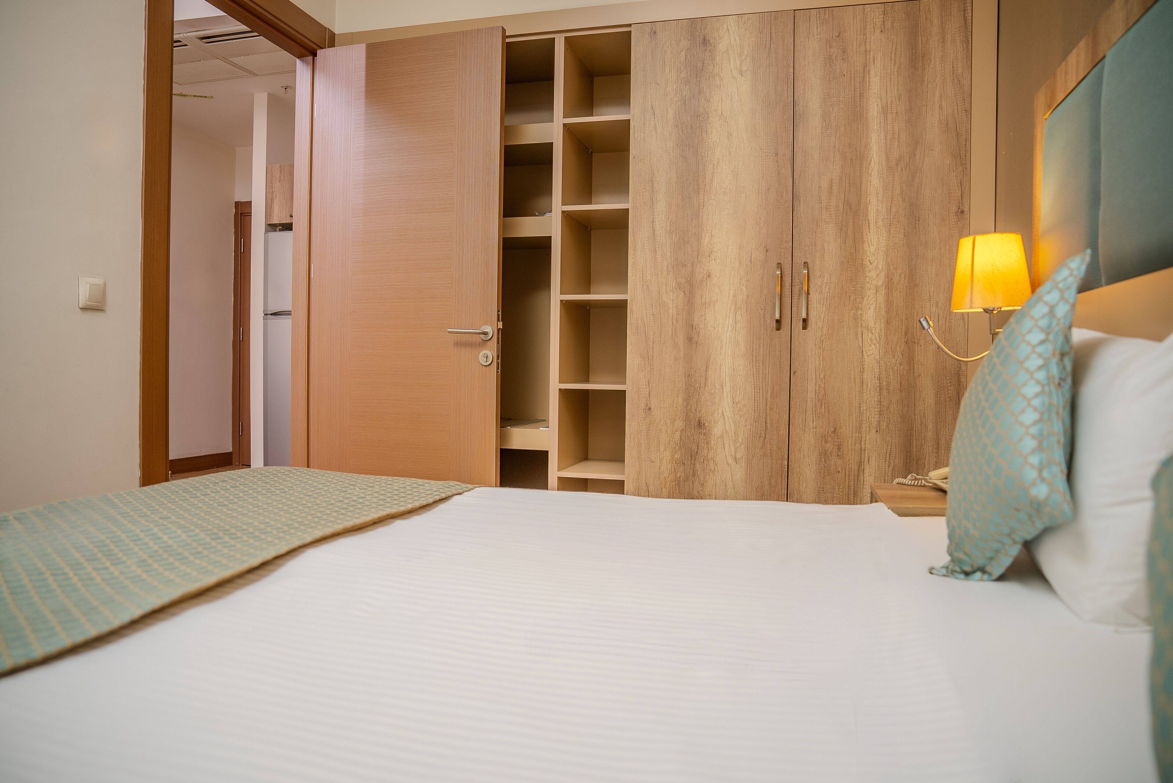Un dormitorio con cama, armario, mesita de noche con lámpara y una pequeña mesa auxiliar.