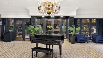 Un hall d’entrée agrémenté d’un grand piano, d’un lustre et de plantes en pot.
