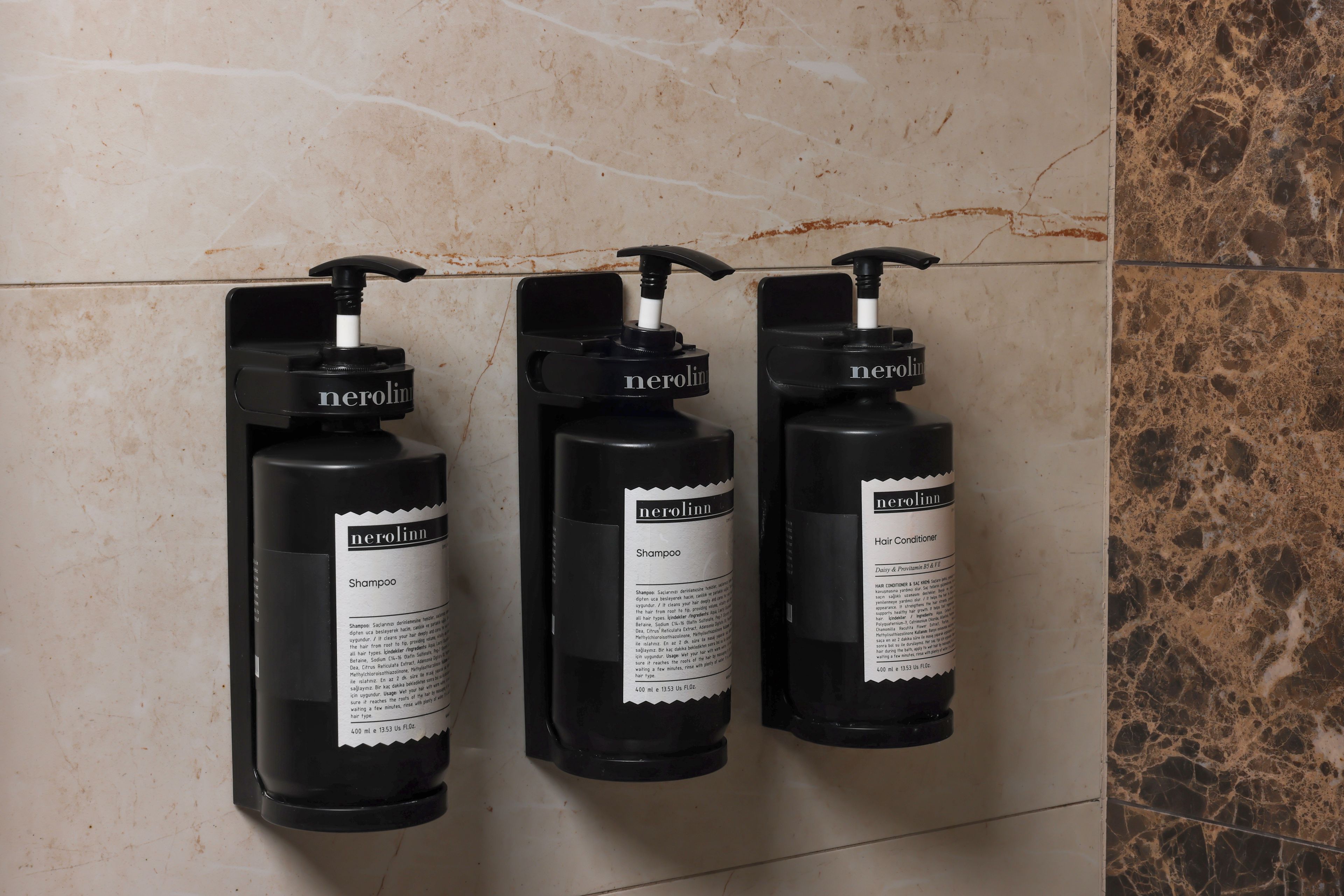 Three black shampoo bottles with pump dispensers labeled 'nerolinn' on a tiled wall.