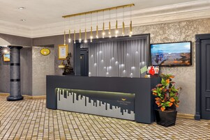 Uma receção com design moderno, um certificado emoldurado na parede e uma televisão a exibir uma vista urbana.