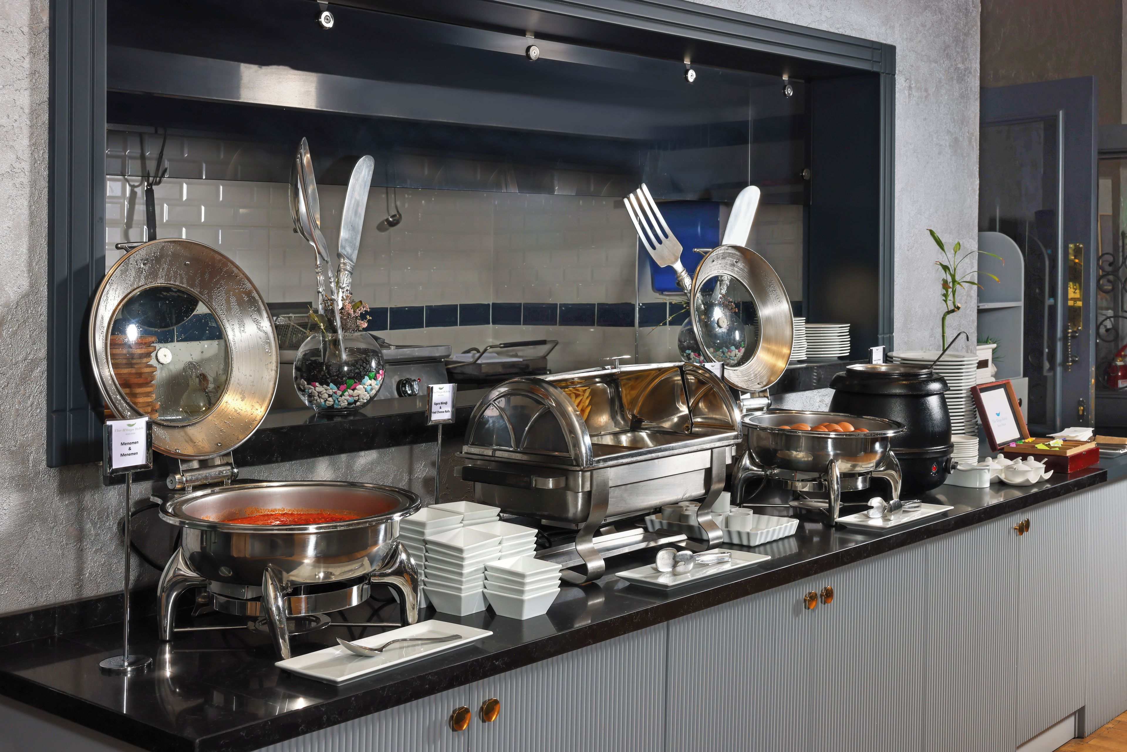 A buffet setup with various food containers, utensils, and a sign indicating 'Menemen & Menemen'.