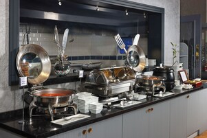 Montaje de bufé con varios recipientes de comida, utensilios y un cartel que indica 'Menemen & Menemen'.