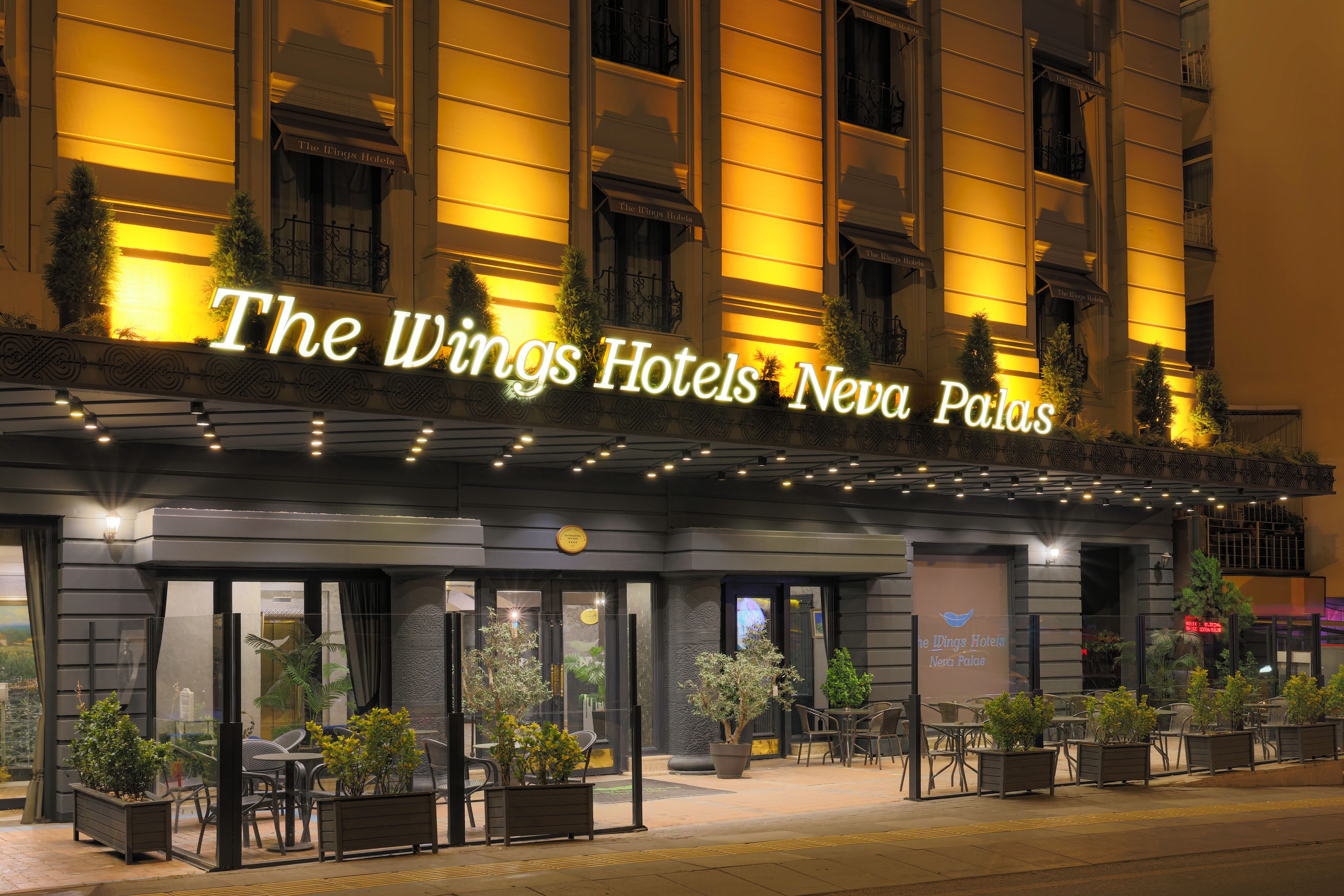 Wings Hotels Neva Palas med en moderne facade, udendørs siddeområde og oplyst skiltning.