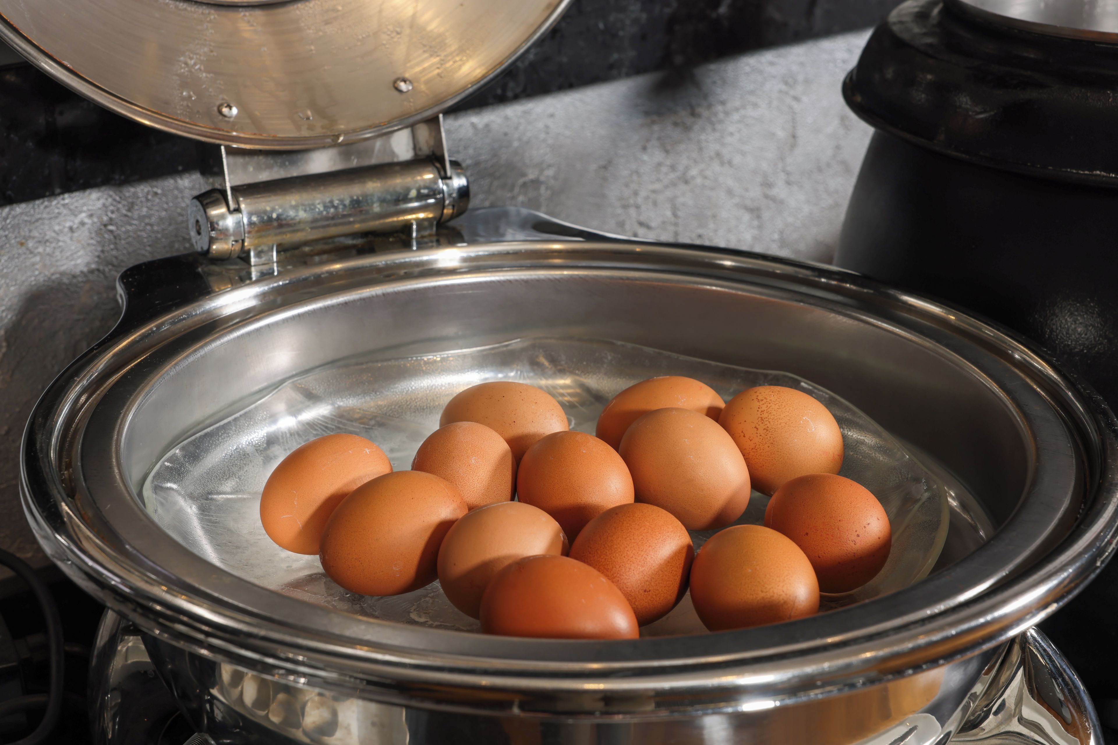 A stainless steel egg poacher with a glass lid containing several eggs.