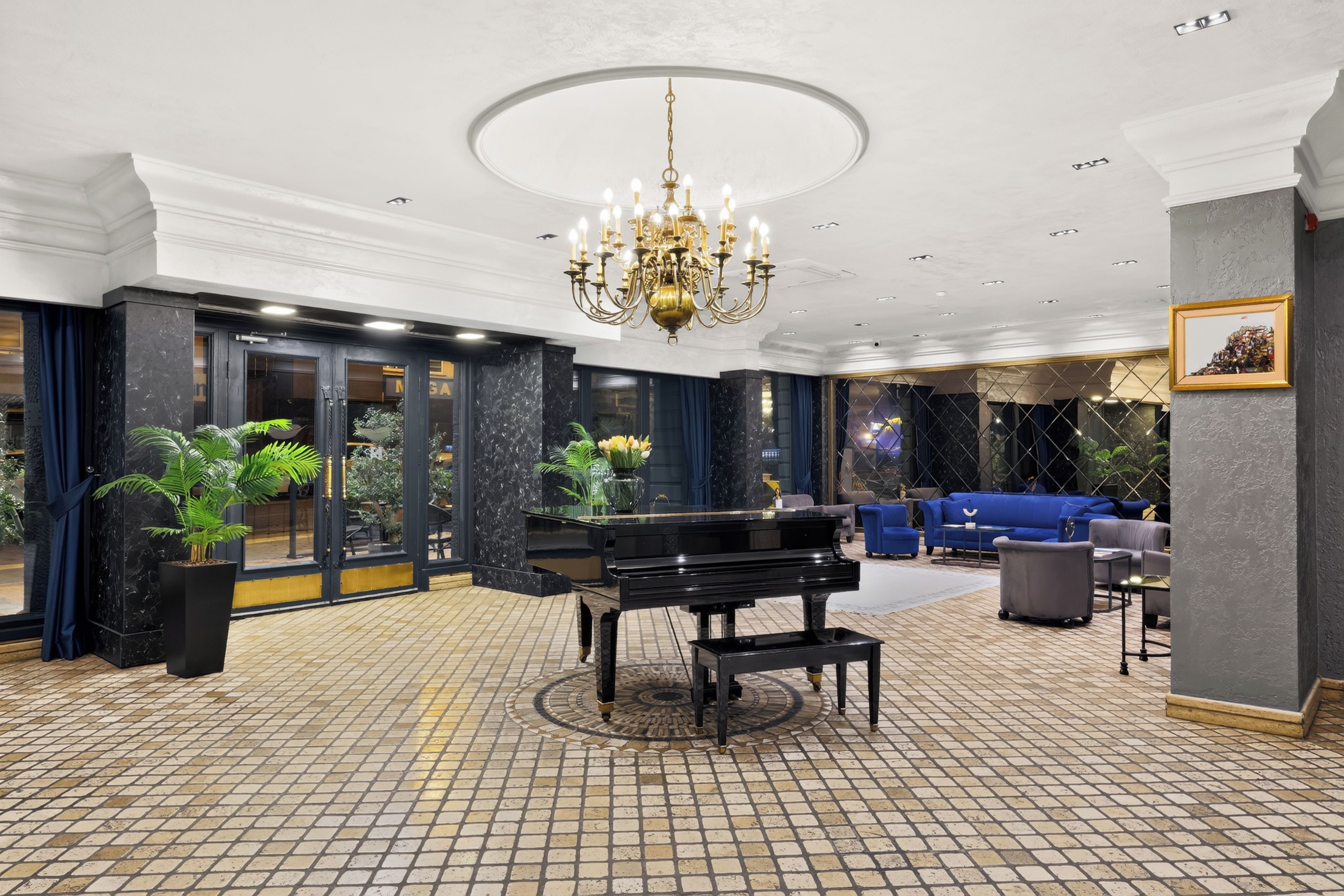 A grand lobby with a black grand piano, a chandelier, and a seating area with blue sofas.