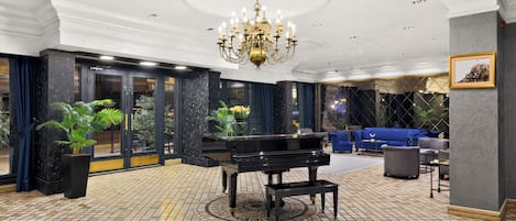 A grand lobby with a black grand piano, a chandelier, and a seating area with blue sofas.