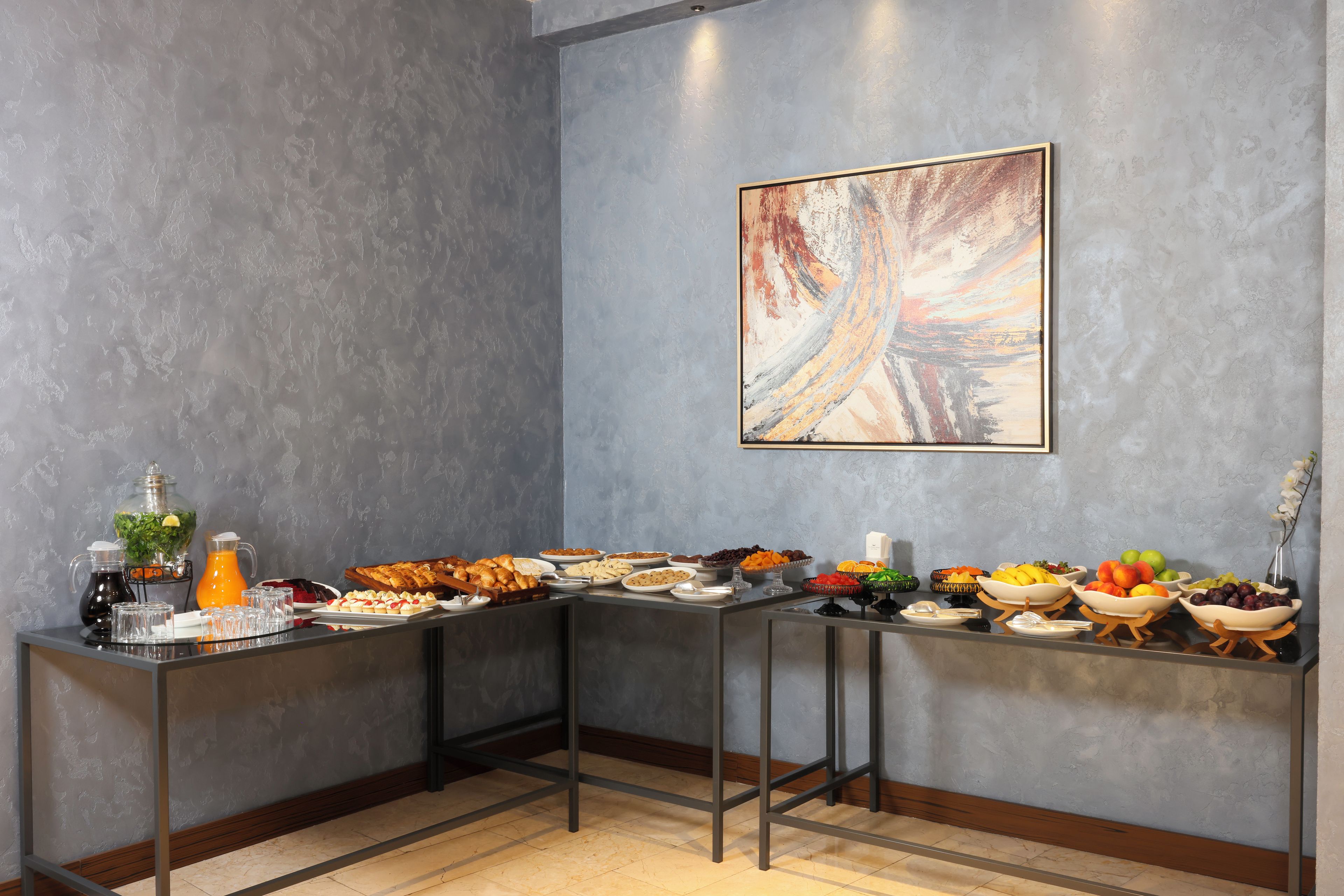 A breakfast buffet with various food items and beverages, a painting on the wall, and a modern interior design.