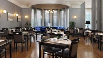 Ein Restaurant mit mehreren Tischen und Stühlen, einem blauen Sofa und großen Fenstern mit Jalousien.
