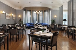A restaurant with multiple dining tables and chairs, a blue sofa, and large windows with blinds. - The Wings Hotels Neva Palas (Ankara)