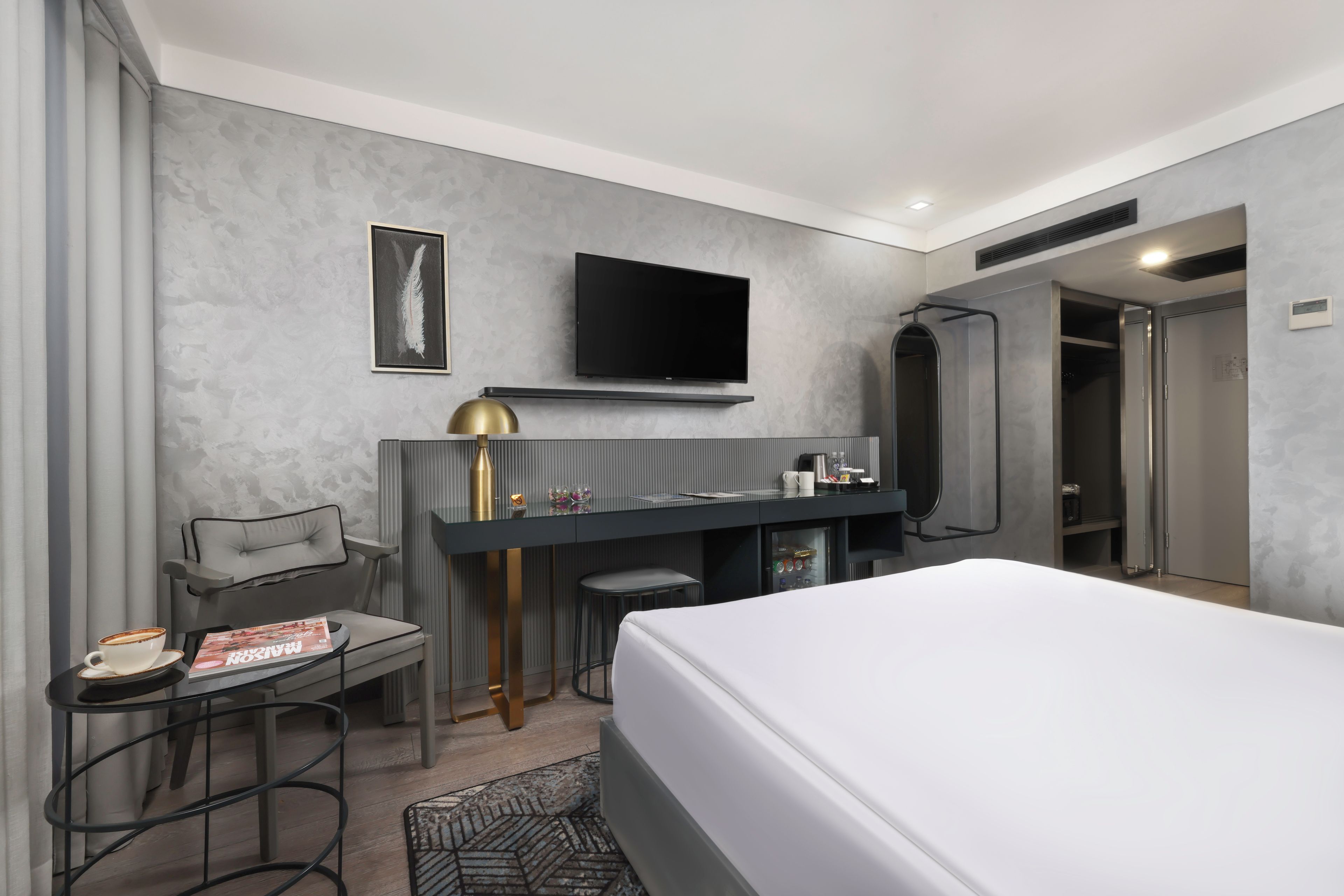 A modern hotel room with a bed, a desk with a chair, a television, and a shower area.