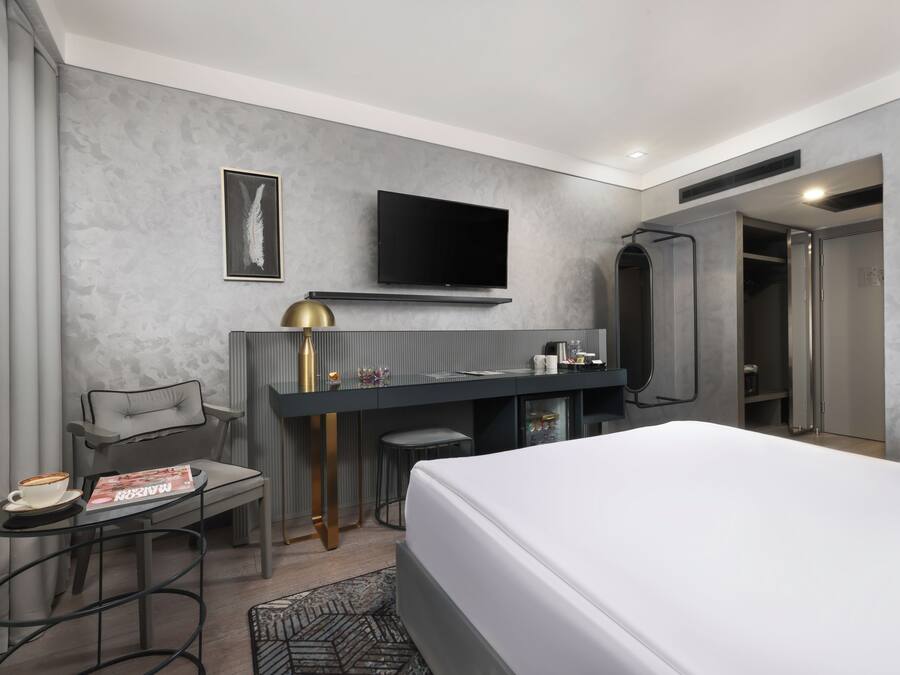 Une chambre d’hôtel moderne équipée d’un lit, d’un bureau avec une chaise, d’une télévision et d’un espace douche.