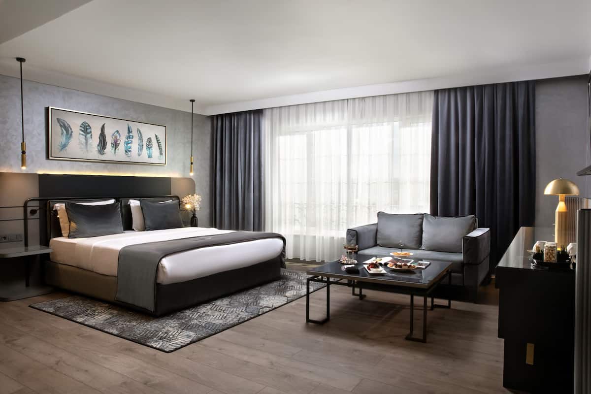 Quarto de hotel moderno com uma cama grande, um sofá, uma mesa de centro e uma escrivaninha com abajur.