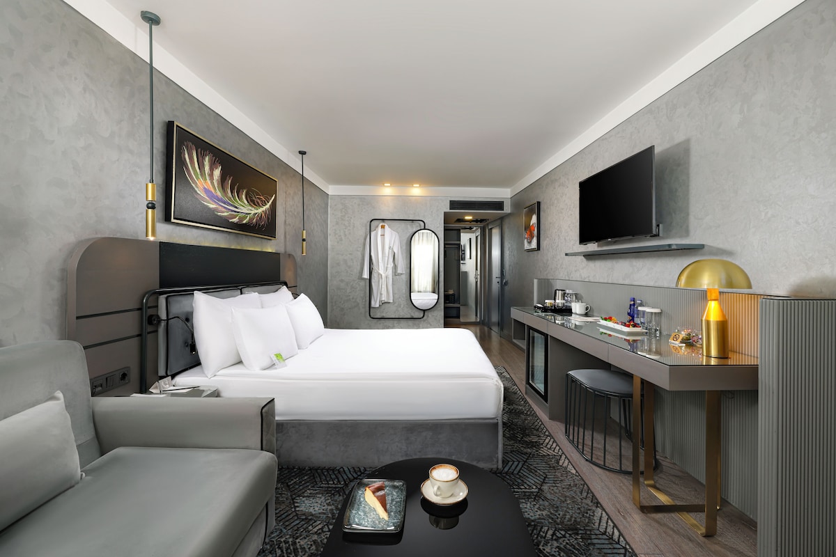 A modern hotel room with a bed, a desk, a chair, a TV, and a coffee table.