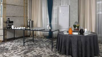 Um quarto com espaço para buffet, estação de café e mesa com dispensador de bebidas.